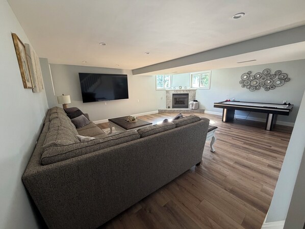 Een moderne woonkamer met een hoekbank, een flatscreen-tv, een open haard en een pooltafel.