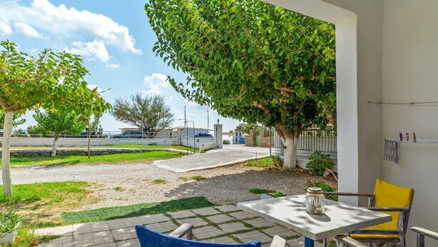 An outdoor patio with a table and chairs, a tree providing shade, and a view of the surrounding area.