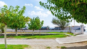 A parking area with trees, gravel, and a white wall.