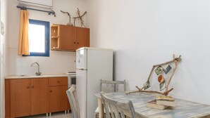 A compact kitchen with wooden cabinets, a white refrigerator, a dining table with chairs, and a window with curtains.