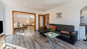 A modern living room with a sofa, coffee table, and a TV. There is a dining area with a table and chairs, and a kitchen area with a countertop. - Apartment "Burmeister" with Private Terrace & Wi-Fi (Nittenau)