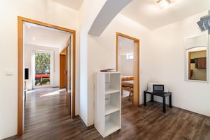 Un interior moderno con piso de madera, una estantería blanca, un microondas sobre una mesa pequeña y una puerta que da a un espacio exterior.