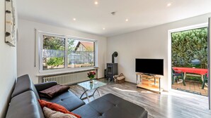 A modern living room with a sofa, a glass coffee table, a fireplace, a TV, and a large window. - Apartment "Burmeister" with Private Terrace & Wi-Fi (Nittenau)