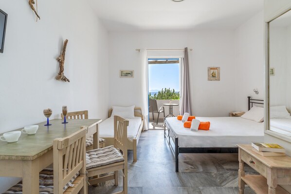 A room with a bed, a desk, a chair, a small table, and a balcony with a view.