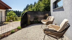Une terrasse avec deux fauteuils en osier, un sol en gravier et une vue sur une zone boisée.