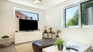 Un salon moderne avec un téléviseur à écran plat, un canapé, une table basse et des plantes en pot.