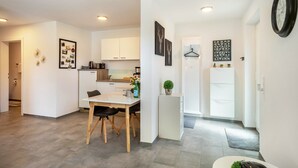 Une cuisine moderne avec des meubles blancs, une table à manger avec des chaises et un petit réfrigérateur.