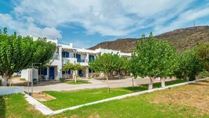 A white building with blue doors and windows, surrounded by green trees and a grassy area. - Holiday Home '1b Kypri Seaview Perasma Studio' with Sea View, Wi-Fi and Air Conditioning (Kypri)
