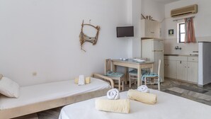 A room with two single beds, a small table with chairs, a TV mounted on the wall, and a kitchenette area. - Holiday Home '1b Kypri Seaview Perasma Studio' with Sea View, Wi-Fi and Air Conditioning (Kypri)