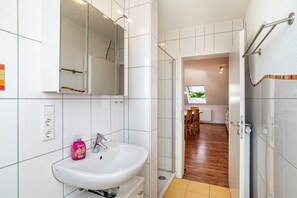 Een badkamer met een wit wastafelmeubel, spiegel en douchehoek.
