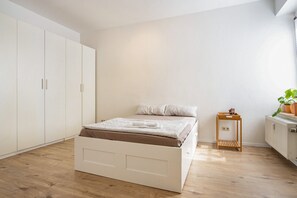 Ein Schlafzimmer mit einem Bett, einem weißen Kleiderschrank, Holzboden und einem kleinen Hocker.