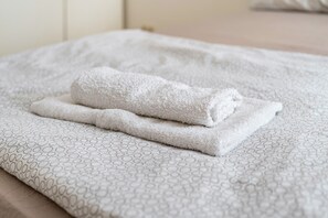Una toalla blanca doblada con cuidado sobre una cama con una colcha estampada.