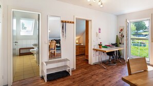 Un interno moderno con pavimento in legno, zona pranzo con tavolo e sedie, angolo cottura con lavello e pensili, e vista su un giardino esterno attraverso una porta vetrata.