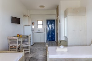 Un dormitorio con cama, escritorio, silla, televisor, armario y baño con lavabo y espejo.