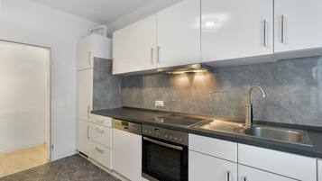 Una cocina moderna con armarios blancos, encimera negra, pileta de acero inoxidable y horno integrado.