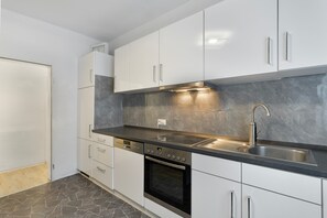 Una cucina moderna con mobili bianchi, un piano di lavoro nero, un lavello in acciaio inossidabile e un forno integrato.