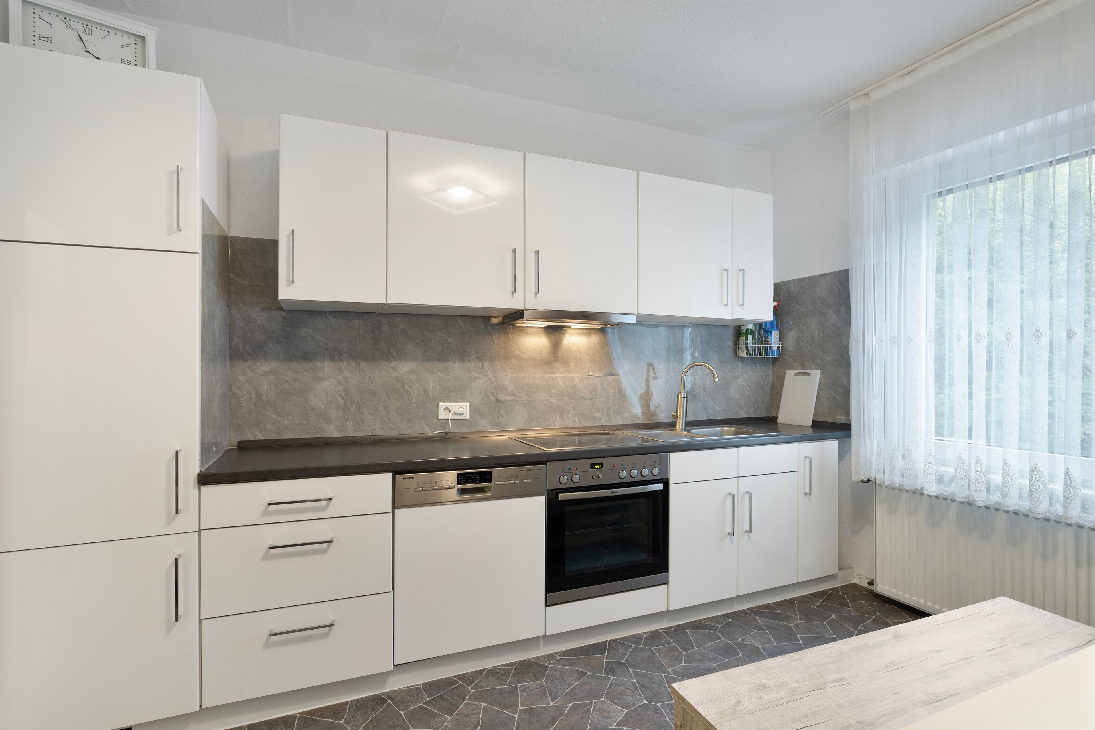 Una cucina moderna con mobili bianchi, forno integrato e pannello di pietra a parete.