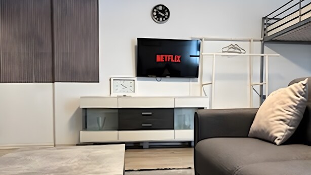 Un salon moderne avec un canapé, un téléviseur fixé au mur, une horloge et un design minimaliste.