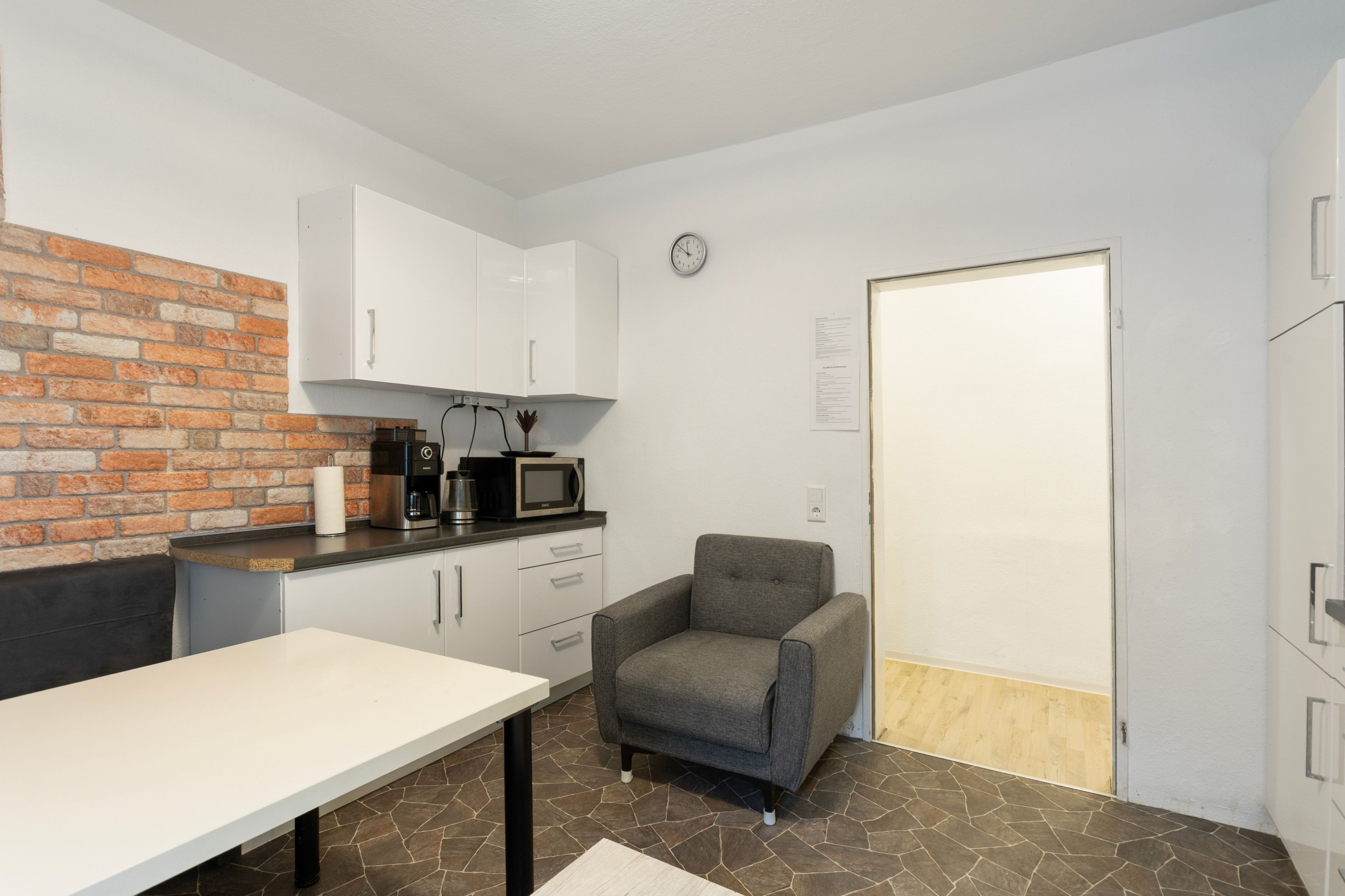 A compact kitchen with a microwave, coffee maker, and a brick wall.