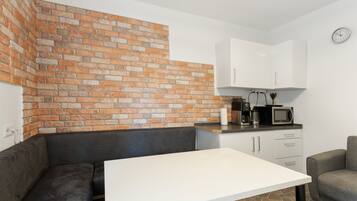 Eine kleine Küche mit Backsteinwand, weißer Arbeitsplatte, schwarzem Sofa und grauem Sessel.