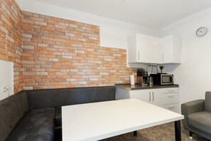 Una cocina compacta con pared de ladrillo, encimera blanca, sofá negro y sillón gris.