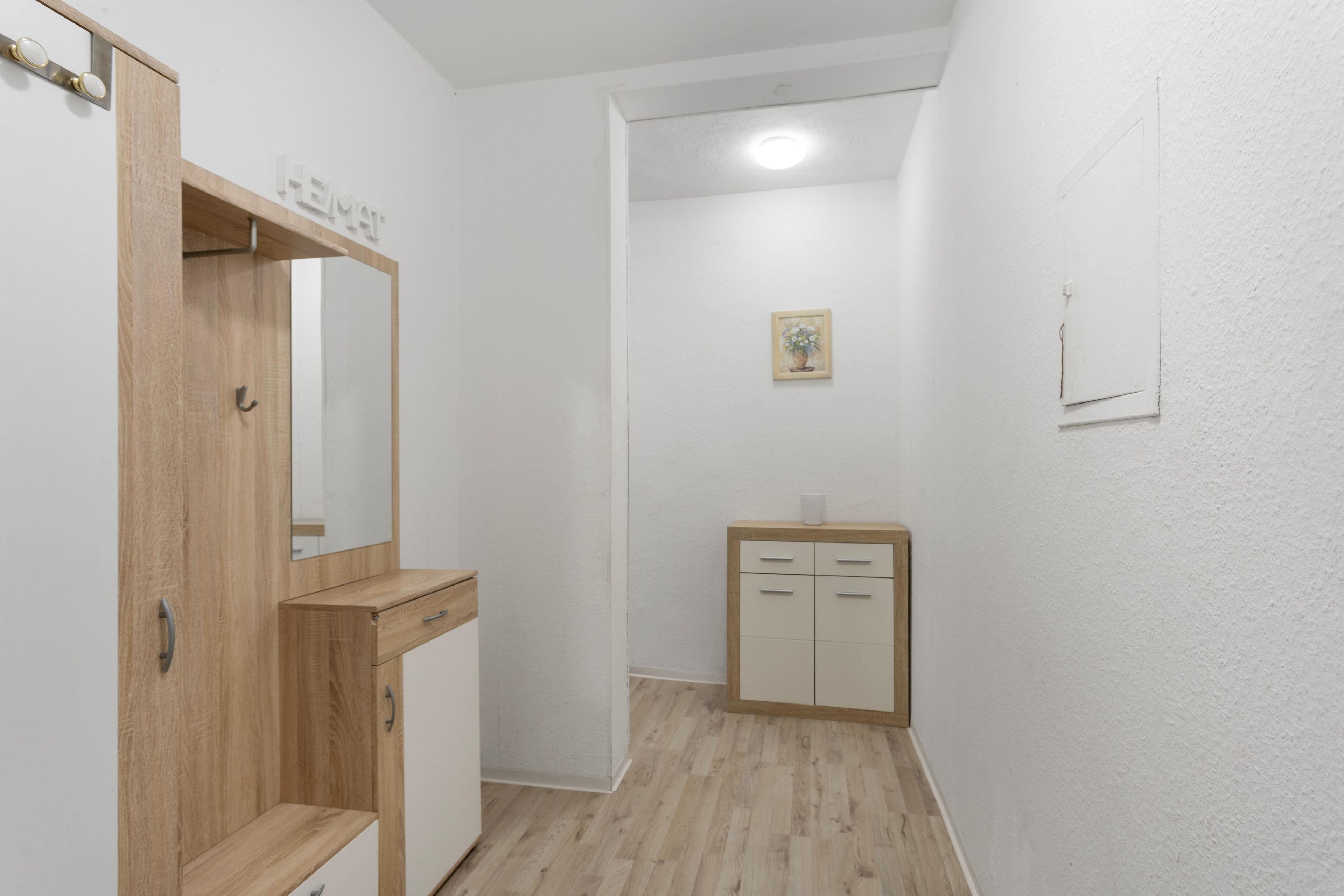 A narrow hallway with a wooden wardrobe, a small cabinet, and a framed picture on the wall.