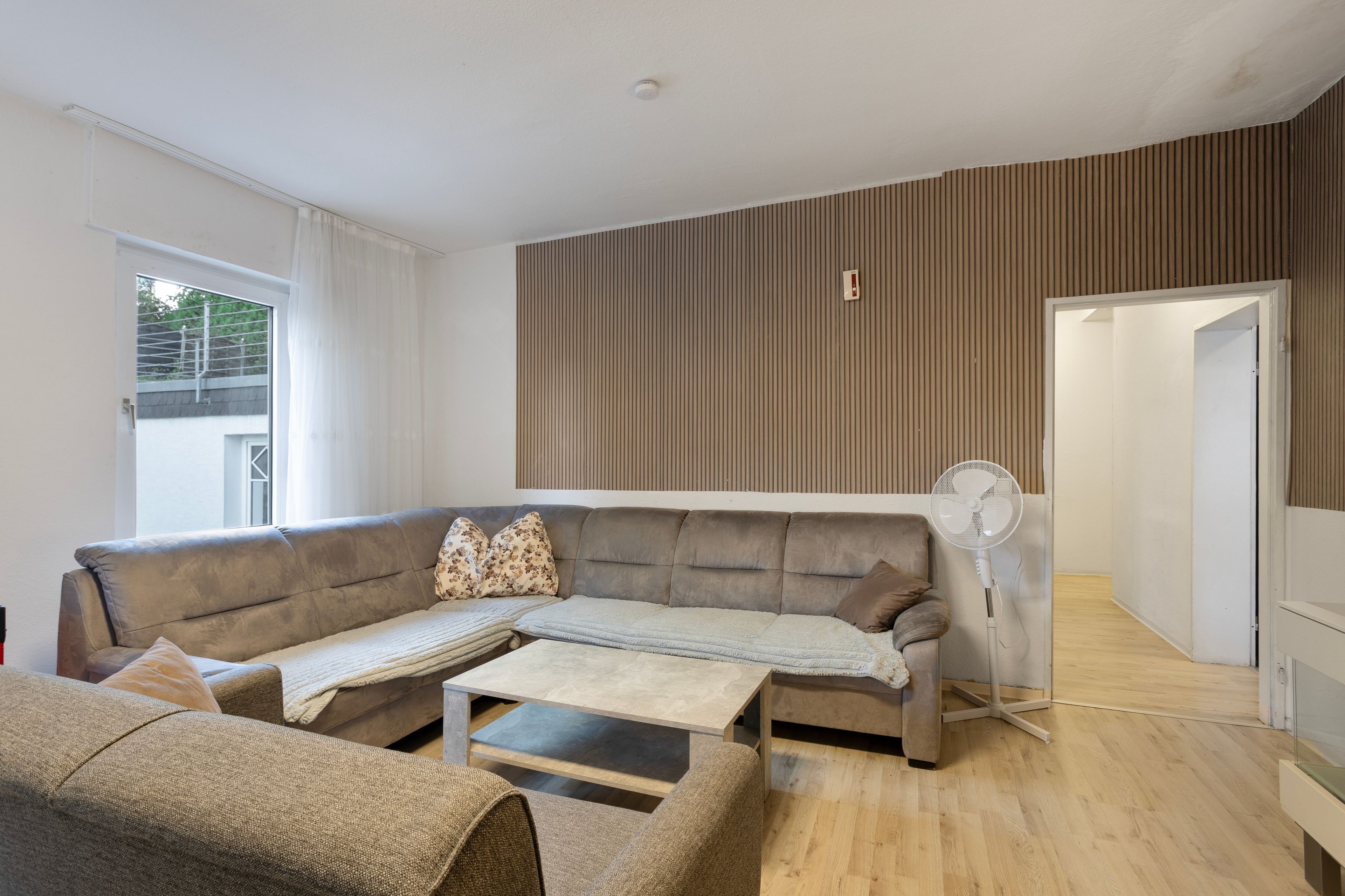 Una sala moderna con un sofá modular, una mesa de centro y un ventilador de pie.