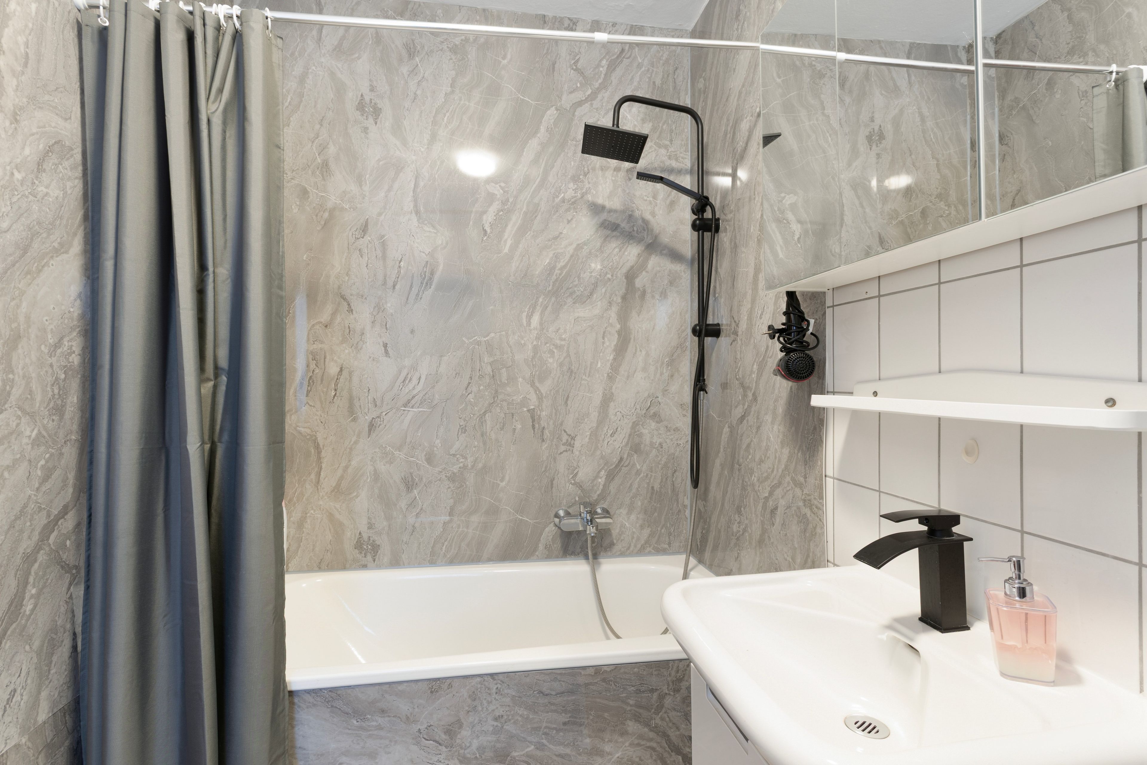 Un baño moderno con ducha, bañera y lavamanos con dispensador de jabón.