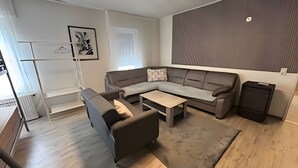 Un salon moderne comprenant un canapé d’angle, une table basse, une petite table, un porte-manteau et une grande œuvre d’art accrochée au mur.