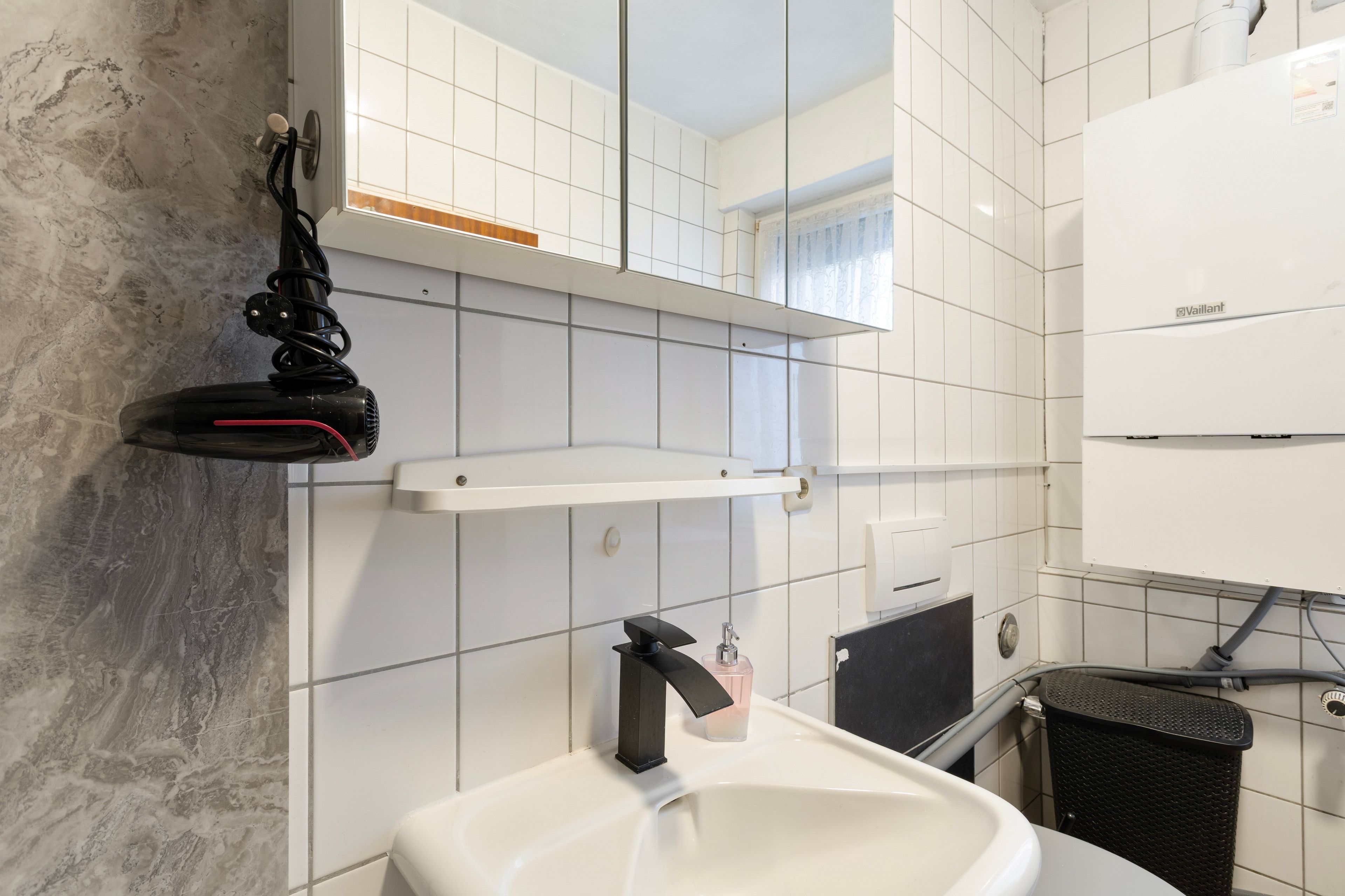 Ein Badezimmer mit weißem Waschbecken, einem Spiegel, einem Handtuchhalter und einer Duschkabine.