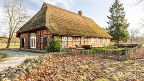 Une maison traditionnelle en bois, avec un toit de chaume, un mur en pierre et un jardin entouré d’une clôture en bois.