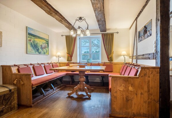 A wooden bench seating area with a central table, wooden beams on the ceiling, and a window with curtains.