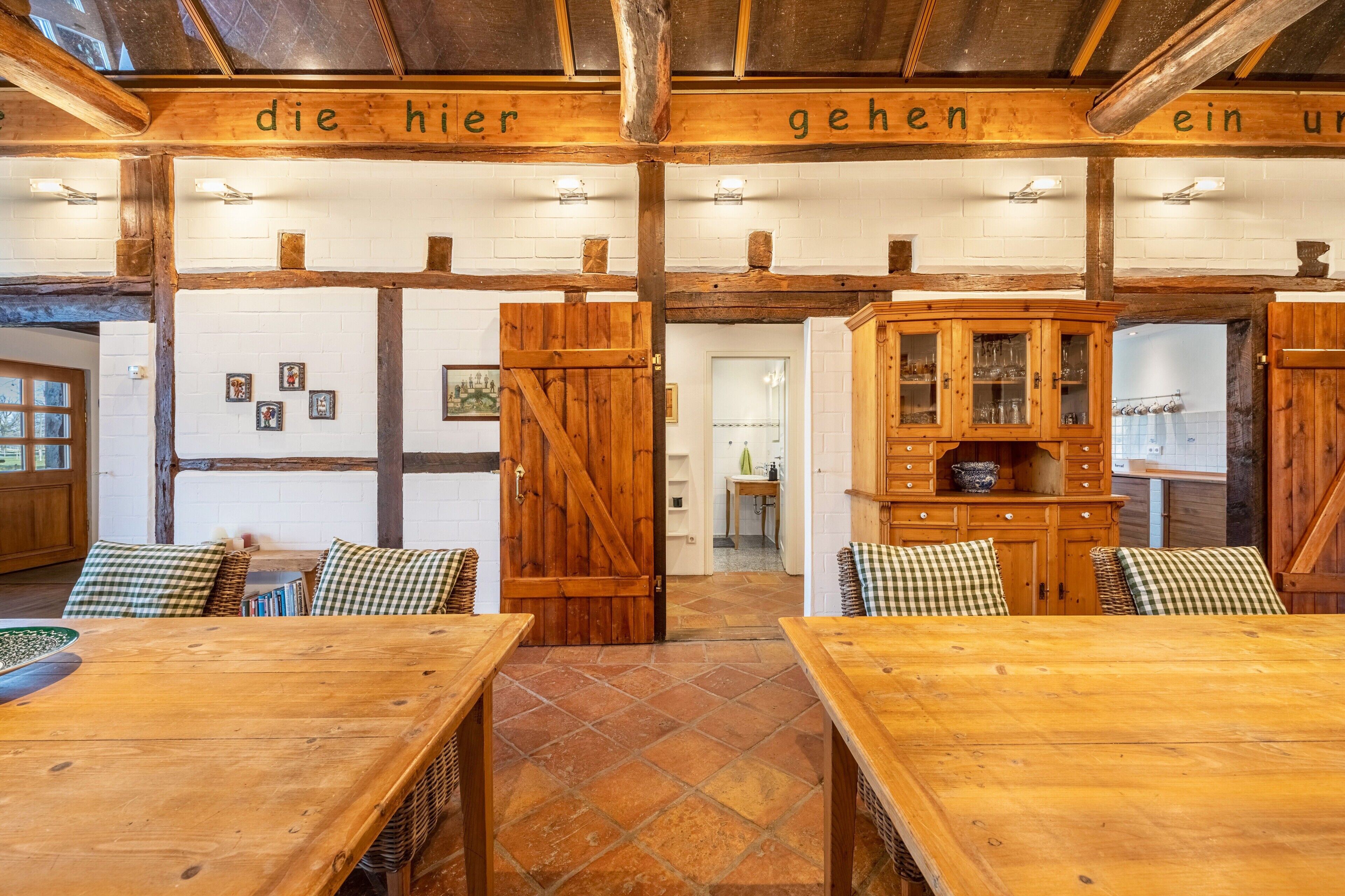 A rustic interior with wooden beams, checkered cushions, and a wooden cabinet with glassware.