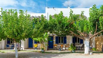 Un bâtiment à l’extérieur blanc, avec des volets bleus et un espace extérieur abrité, aménagé avec des tables et des chaises.