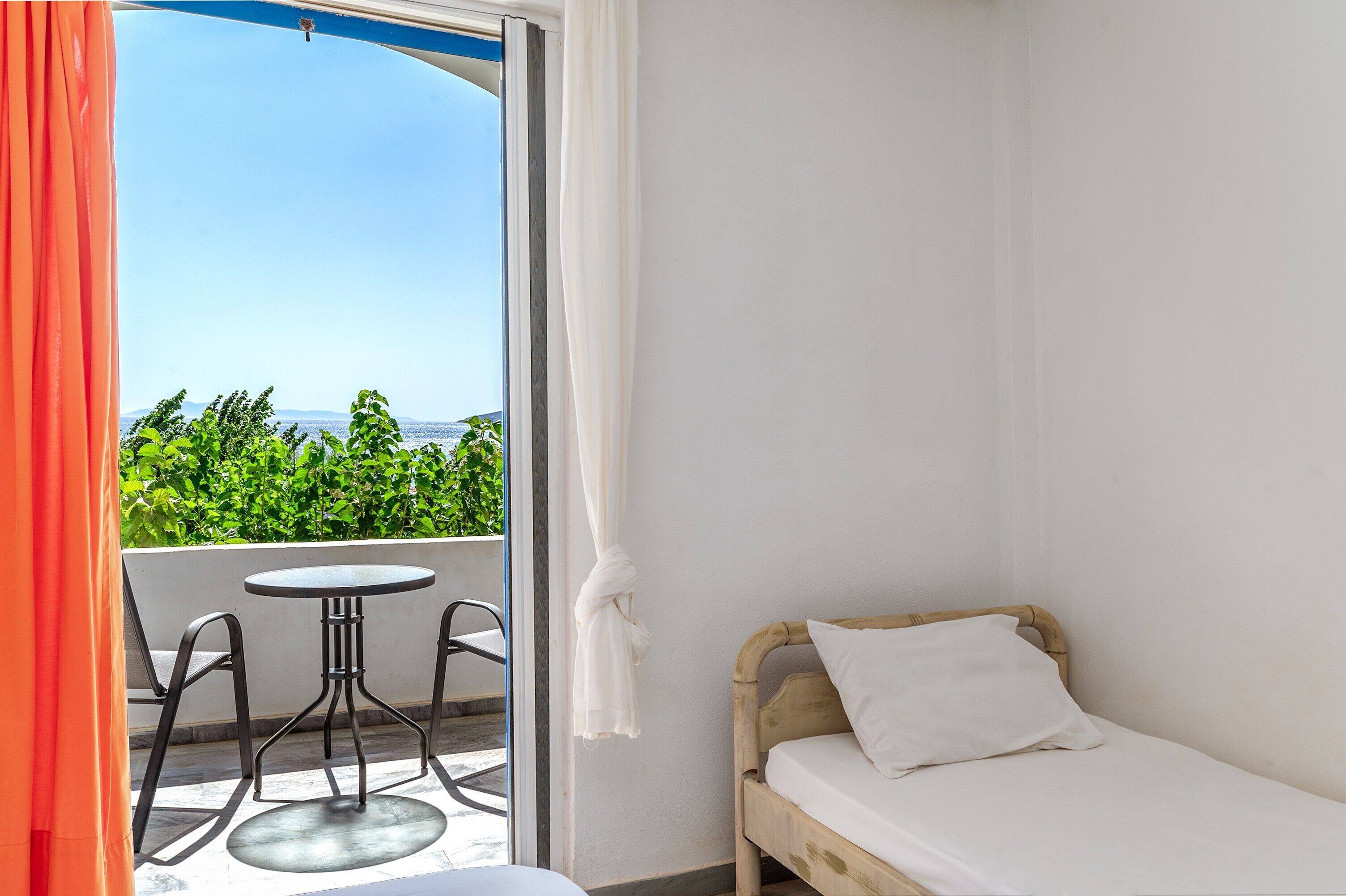 Une chambre avec un lit, une table et des chaises, et un balcon offrant une vue sur la verdure et la mer.