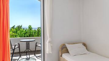 Une chambre avec un lit, une table et des chaises, et un balcon offrant une vue sur la verdure et la mer.