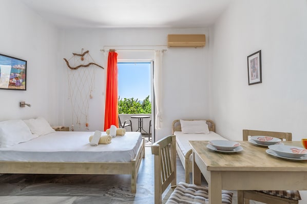 A room with two beds, a dining table, a small balcony, and a window with curtains.