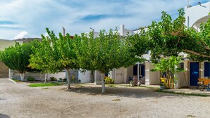 A courtyard with a gravel ground, trees, and a building with a blue door. - Holiday Home '6 Kypri Seaview Perasma Studio' with Sea View, Wi-Fi and Air Conditioning (Kypri)