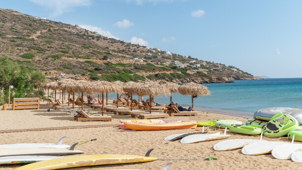 A beach with sun loungers, umbrellas, and surfboards.