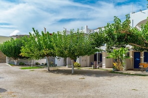 A courtyard with a gravel ground, trees, and a building with a blue door. - Holiday Home '5 Kypri Seaview Perasma Studio' with Sea View, Wi-Fi and Air Conditioning (Kypri)