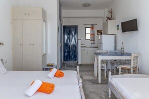 A hotel room with two beds, a dining table, a kitchen area, and a TV mounted on the wall.