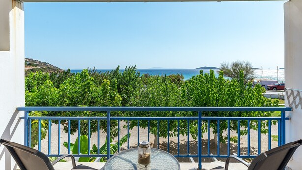 A balcony with a view of the sea, a table with a glass jar, and a blue railing.
