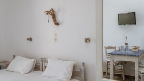 A bedroom with a bed, bedside table, wall-mounted TV, and a mirror reflecting a dining area with a table and chairs.