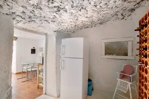 Una cocina compacta con un refrigerador blanco, una ventana pequeña y una silla con cojín a rayas.