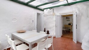 A white interior with a table and chairs, a ceiling fan, and a door leading to another room.