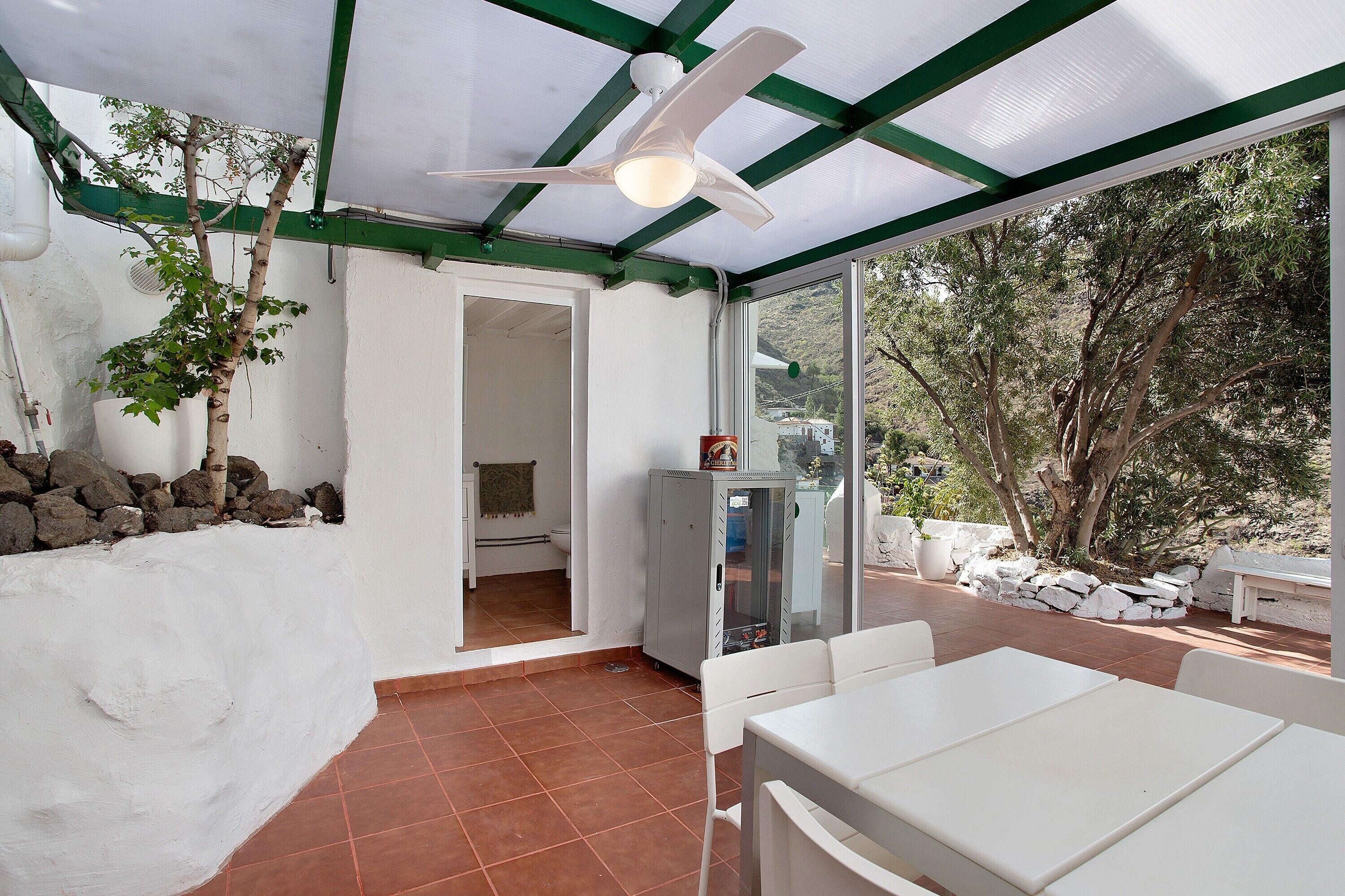 Portico coperto con ventilatore a soffitto, pareti bianche, pavimento piastrellato e vista sul giardino.