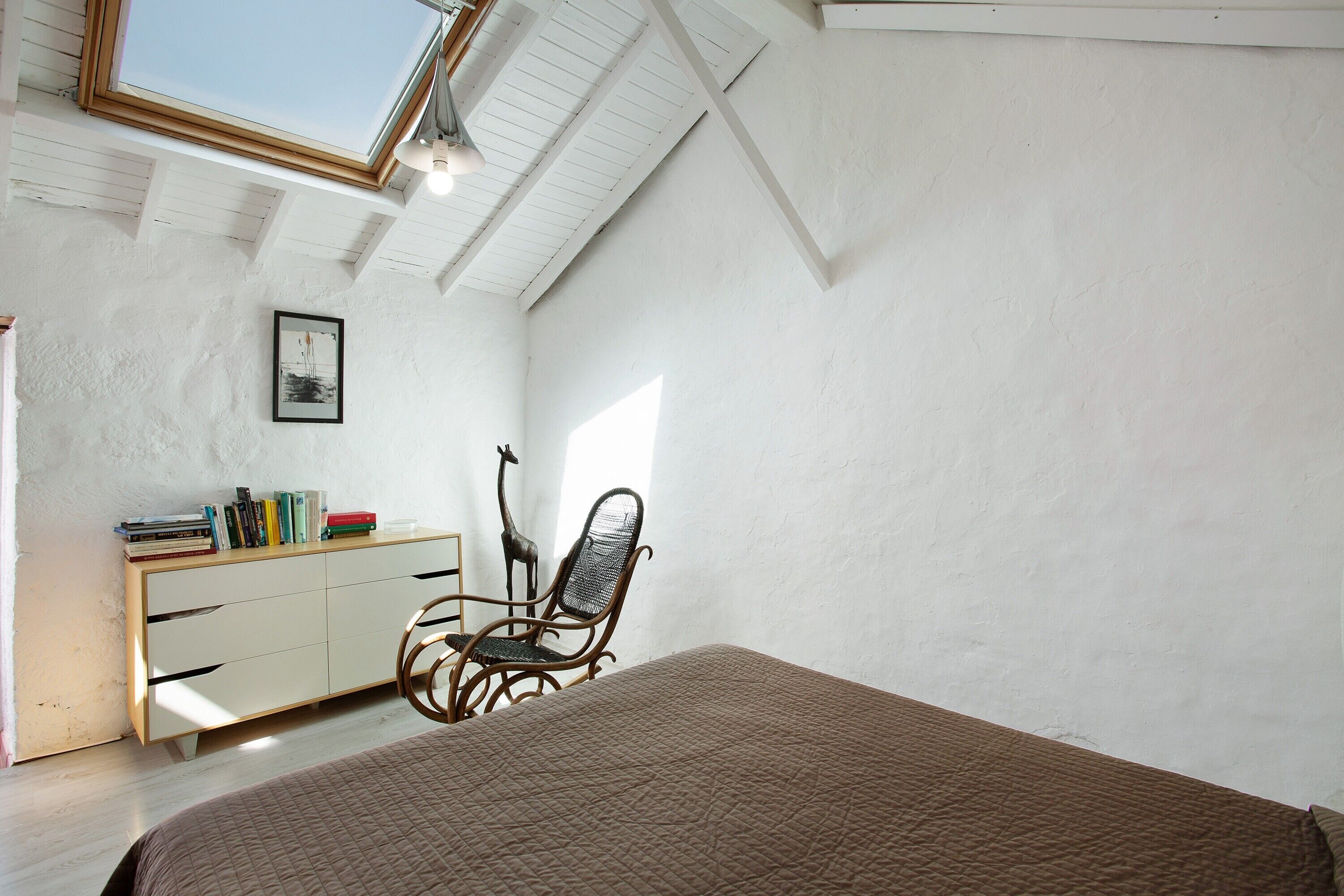 Un dormitorio con una cama, un escritorio con libros, una estatua de jirafa y un tragaluz.