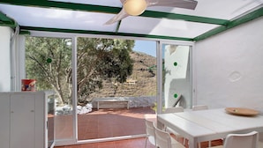 A room with a sliding glass door leading to an outdoor patio, a white table with chairs, and a ceiling fan.