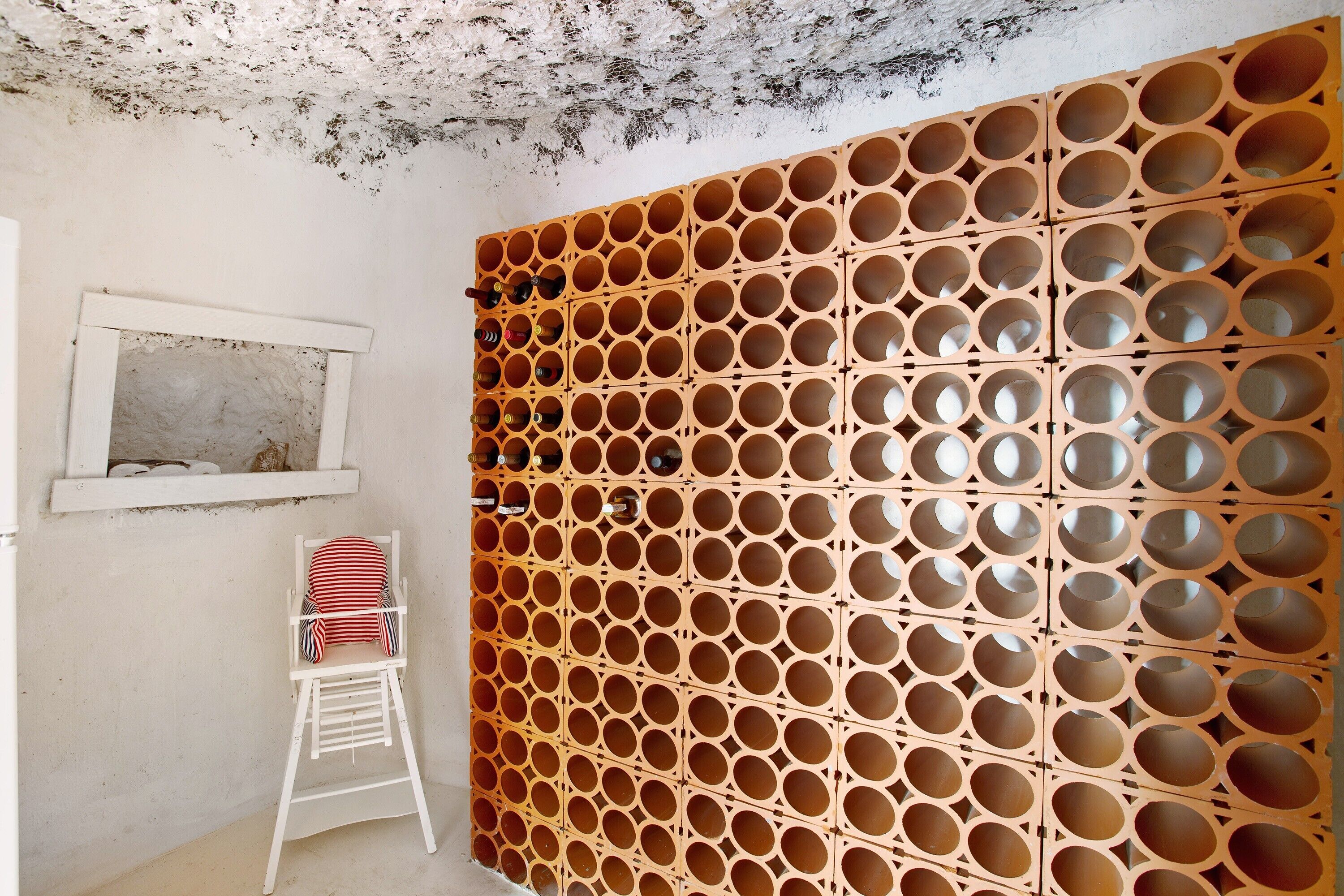 A room with a white wall, a wooden partition with circular cutouts, a white chair, and a small window.