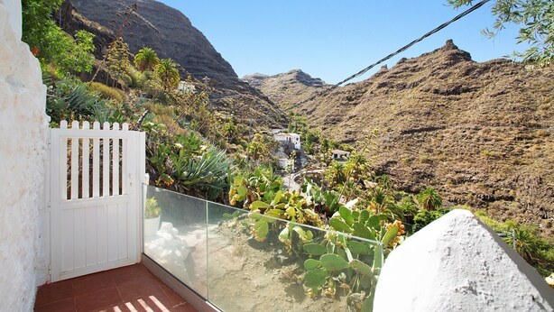 A balcony with a view of a mountainous landscape, a white gate, and a glass railing.